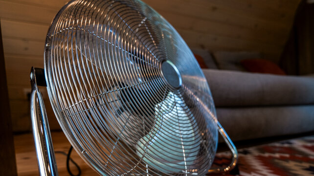 Close-up of a chrome floor fan in a cozy living room with a sofa in the background