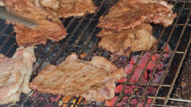 Macro view of sizzling pork chops with bubbling fat on a street food charcoal grill, featuring dynamic flames