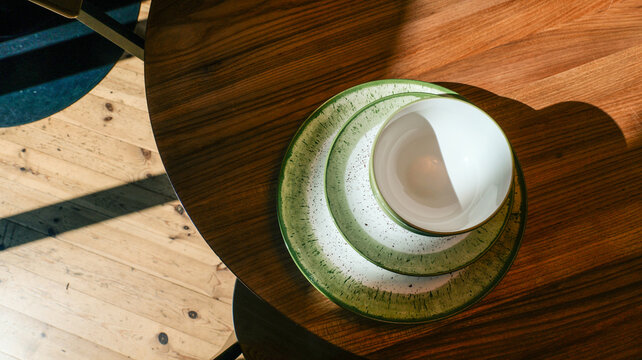 Stack of rustic green speckled plates and white bowl on a wooden table