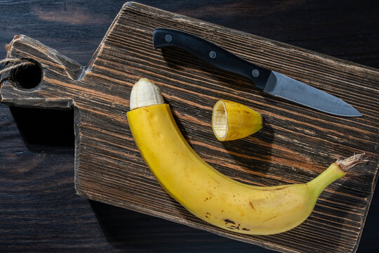 Circumcision concept with cut banana skin and kitchen knife. Conceptual metaphor for male circumcision procedure showing cut yellow banana. Healthcare and medical education photography