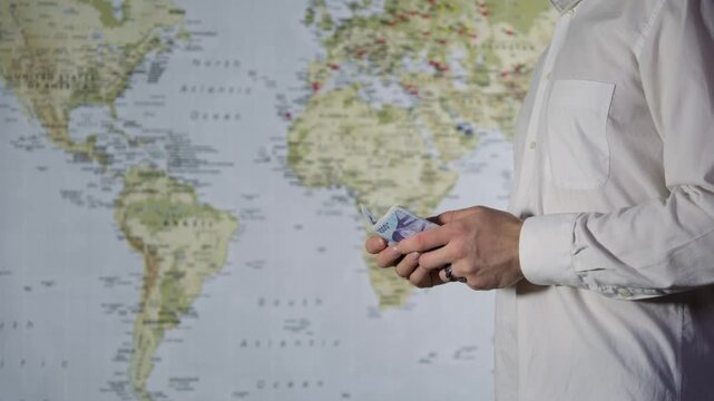 Close-up of a man in a white shirt counting cash won against a world map