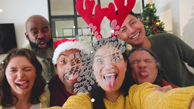 Woman yellow sweater raising phone, causing AR snow, group leaning in capturing holiday selfie