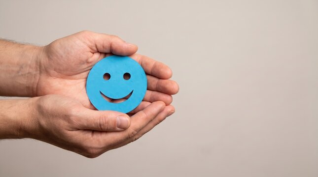 Hands Holding Blue Paper Cutout of Happy Smiley Face in Studio, Symbolizing Positive Mental Health, Emotional Wellness, and Psychological Support Concepts