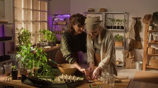 Senior Caucasian woman and young Caucasian woman discussing seed packets and planting seeds in indoor nursery. Ideal for sustainable lifestyle and home gardening advertisements