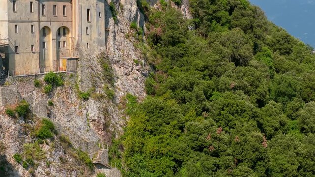 Greccio Monastery Sanctuary Lazio Italy 4K Drone. 70mm vertical rise reveal flight from below cliff face with downward camera tilt. Franciscan hermitage historic b roll cinematic video asset
