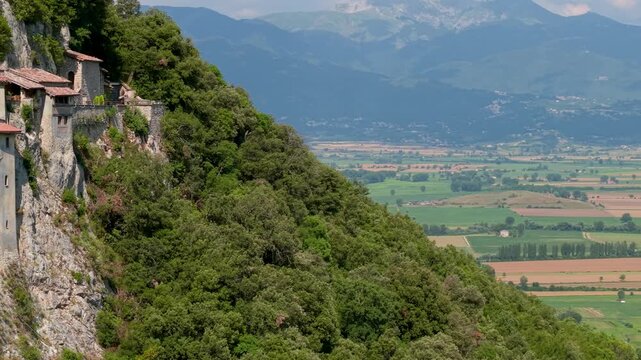 Greccio Monastery Lazio Italy 4K Drone. 70mm pan left to right from cliffside sanctuary to green valley with fields and mountain background. Most beautiful villages cinematic establishing shoot