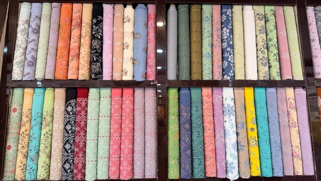 Colorful Pakistani fabric store shelves with patterned and embroidered unstitched dress materials.