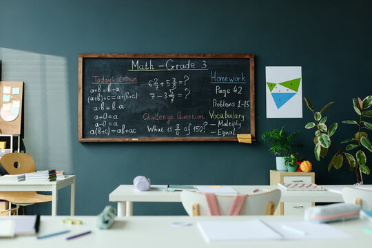 Wide shot of elementary classroom displaying grade 3 math lesson on chalkboard, presenting fractions, homework, vocabulary, learning concept. Useful for education marketing, school content