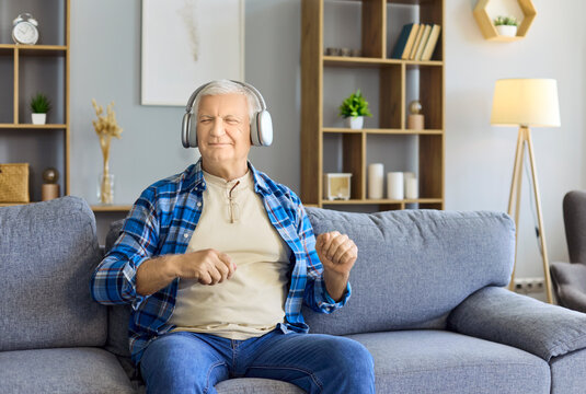 Senior man with headphones on sofa enjoying music. Smiling retiree relaxes in a cozy living room, eyes closed, enjoying rhythm and calm for wellness ads. Concept of relaxed home leisure.