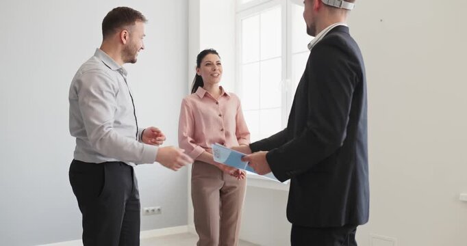 Couple with agent in apartment viewing. They consult with a broker and inspector in hardhat about purchase terms, financing, and contractor timelines. Clear real estate discussion concept.