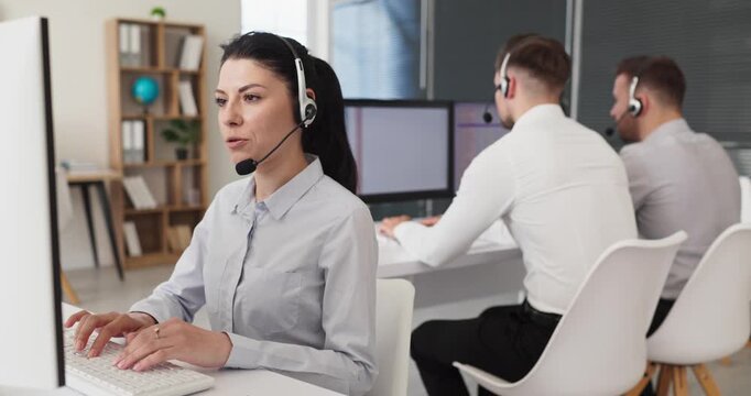 Operator support agent with headset in office. Focused female handles customer call at helpdesk, resolving issues with clear communication. Customer service communication teamwork concept.
