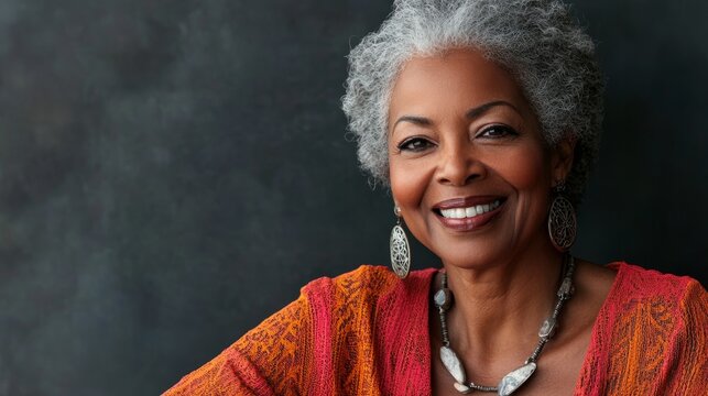 African American woman with gray hair, wearing vibrant orange top, smiling warmly against a textured background, showcasing confidence and joy in a portrait setting