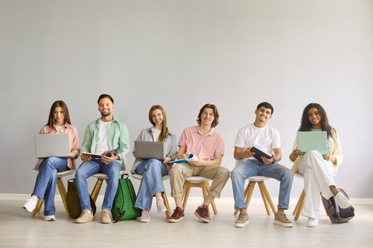 Students group in classroom with laptop studying. Six smiling students sit together, learning with laptops and notebooks, showing college teamwork. Strong concept of teamwork and education.