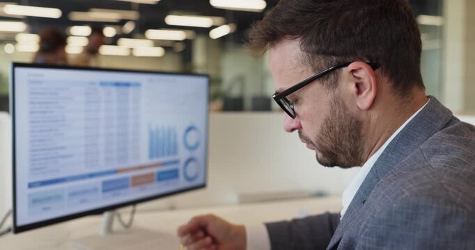Analyst businessman reviews spreadsheet charts and data. Manager at office computer reviews finance reporting to gauge trends, check accuracy for planning. Clear finance data analysis concept.