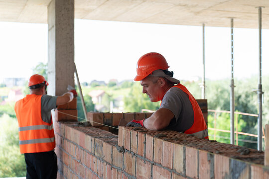 Workers carefully remove excess mortar from joints in bricks. Builders use special work tool to form smooth and polished material structure