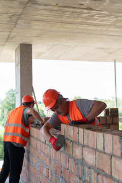 Workers take away unnecessary mortar from brick joints to maintain quality construction. Builders clean construction lines with tools. Vertical shot