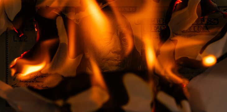 US one hundred dollar bill burning in fire with flames and charred edges close up