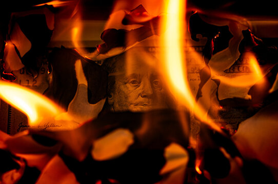 US one hundred dollar bill burning in fire with flames and charred edges close up