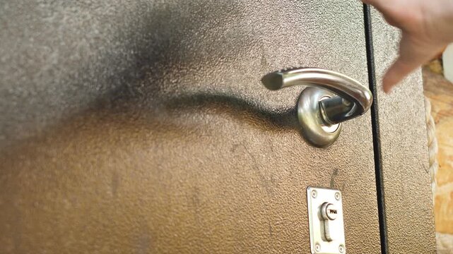 A close-up shot of a hand pressing a metal handle of a heavy entrance door. A person smoothly opens a brown armored door of a country log house