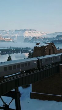 Vertical video: Entering yellow loco with silver cars crossing trestle toward mountains, calm river