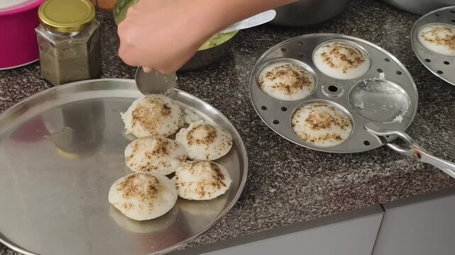 Fresh homemade idlis being carefully unmolded and served with coconut chutney, capturing the authentic preparation of a traditional South Indian breakfast in a home kitchen.