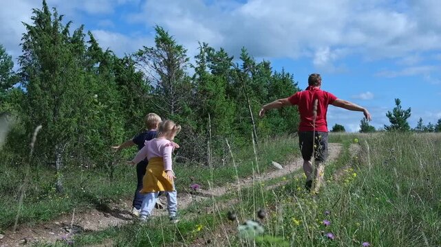 Father walking with his two little children in summer forest. Dad hiking with son and daughter on green grass field, weekend outdoor adventure activity theme. Active Family Lifestyle. Nature Escape
