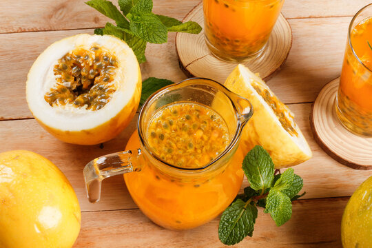 Fresh passion fruit juice served in a glass pitcher with whole and sliced ​​passion fruits, mint leaves and rustic wooden background