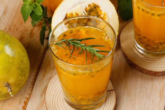 Passion fruit juice made with natural pulp, garnished with rosemary and whole passion fruits, set against a wooden background