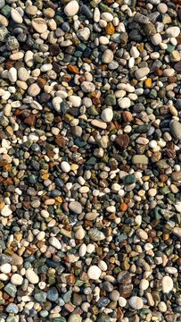Top view of mixed beach pebbles and small stones, natural gravel texture with gray tan and white tones, coastal background for design and nature themes