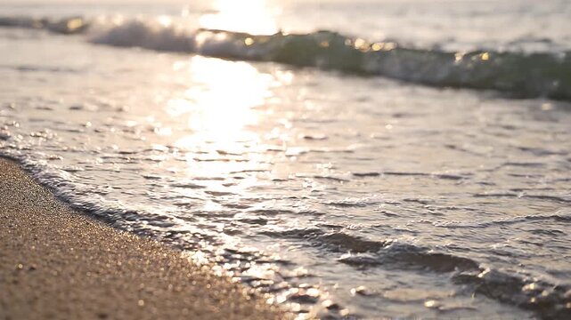 Close up of gentle sea waves washing over sandy beach during golden hour sunset