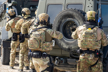 Fototapeta premium Armed Special Forces Soldiers in Camouflage Tactical Gear Storming Armored Vehicle During Military Training Exercise or Combat Operation