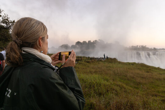 woman taking pictures  of Victoria Falls at sunrise from the Zimbabwe side, Zimbabwe, Africa