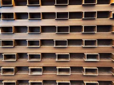 Composite wood wpc brown panel louvers with repetitive rectangular hollow gaps creating an interior wall geometric pattern.