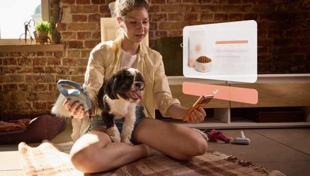 Woman managing dog food order from mobile app while holding small pet at home. Concept of smart pet nutrition, subscription delivery, automatic replenishment and convenient pet ownership.