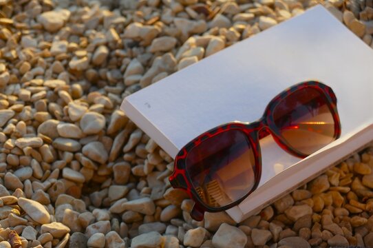 Book and glass on the beach with pebbles by the sea in golden sunset, summer accessories background