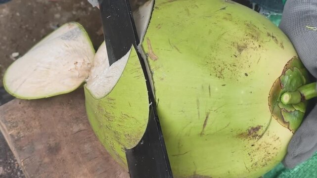 Extreme close-up of a sharp machete chopping a large fresh green coconut, Vietnamese street food preparation