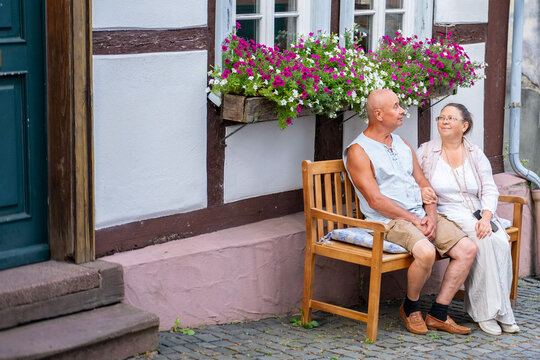 happy senior couple resting wooden bench, Taking time together historic European german village, mature woman man romantic vacation, relaxed lifestyle, travel memories, traditional half timbered house