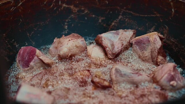 Meat chunks frying in hot oil inside a large wok. Professional cook preparing raw beef for traditional dish. Culinary process of searing food in saucepan pan.