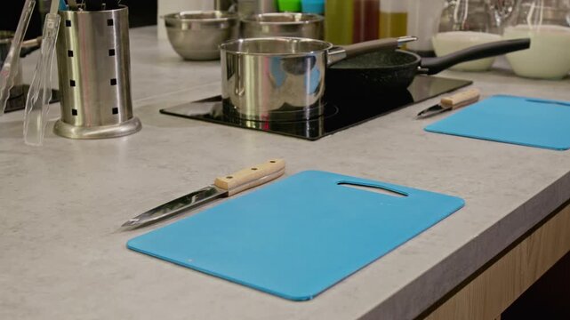 Kitchen counter showing blue cutting boards, knife, and stainless steel pots during slow camera pan. Video is suitable for culinary school promos, cooking show intros, or kitchenware marketing