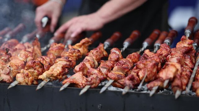 Cook grilling meat skewers on coal brazier. Professional chef preparing barbecue pork shashlik over open fire. Culinary process of outdoor food preparation event.