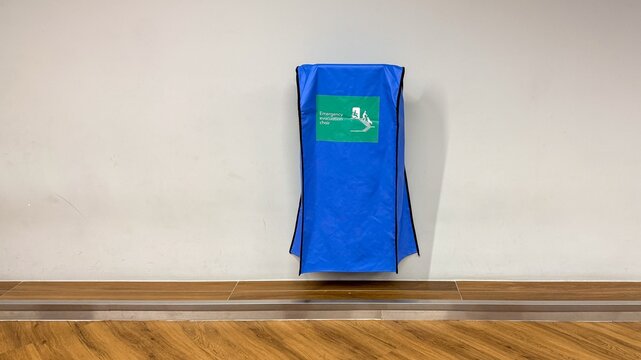 Blue wall mounted emergency kit cabinet in a clean hallway, centered against a white wall with wood floor, conveys readiness and safety for schools offices and gyms
