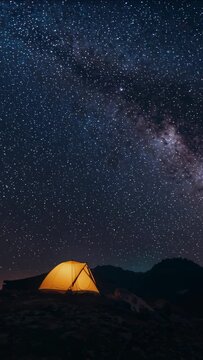 Vertical video: Starting timelapse filming amber tent lit on ridge to capture Milky Way, copy space