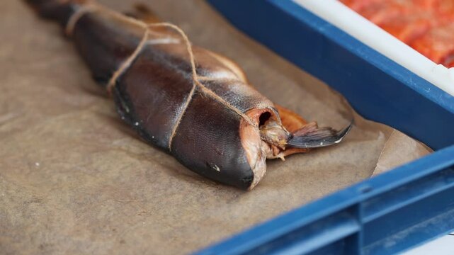 Smoked fish placed in a blue plastic crate. Culinary preparation of gourmet seafood product for retail sale. Traditional artisan food processing industry show.
