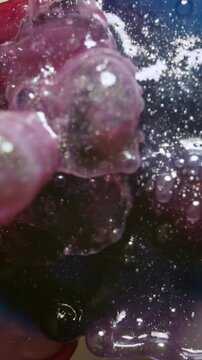 Vertical video: Colliding red-blue drops forming purple mass on white, bubbles sparkling