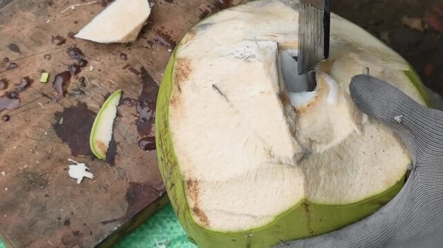 Close-up high-angle shot of a street vendor's machete cutting the top off a fresh green coconut on a wooden board, Vietnamese street food preparation