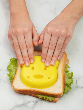 Child hands using yellow cutter mold to shape figure from bread sandwich on marble background top view
