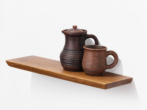 Handmade clay jug with lid and ceramic mug on wooden oak shelf on white wall ethnic home decor