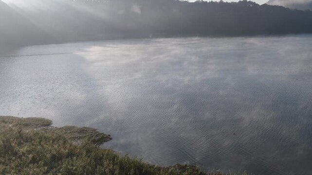 Beautiful cinematic footage of misty Tuyen Lam Lake covered in thick fog during morning sunlight in Dalat, Central Highlands, Vietnam. A serene nature landscape with sun rays reflecting on the water