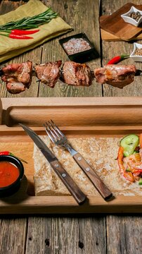 Grilled meat skewers on a rustic wooden table with chili peppers and herbs, served with sauce and a fresh salad, warm casual mood for outdoor dining