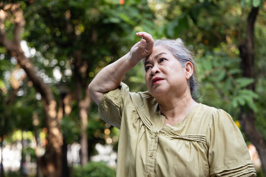 Elderly asian senior woman tired, flushed and sweating from excessive summer heat outdoors, wiping her sweat droplet with discomfort feeling